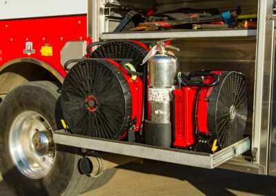 Three BlowHard PPV fans sit in an open tools compartment of a firetruck, wedged around a fire hydrant, showcasing their compact size and portability.