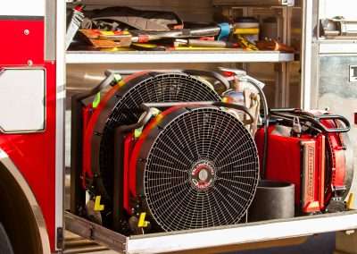 Three BlowHard PPV fans sit in an open tools compartment of a firetruck, showcasing their compact size and portability.