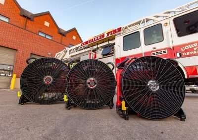 BlowHard's Commando, Quickee, and Squirt fan models lined up in a row in front of a Corvallis Fire Department fire truck and fire station.