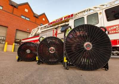 BlowHard's Commando, Quickee, and Squirt fan models lined up in a row in front of a Corvallis Fire Department fire truck and fire station.